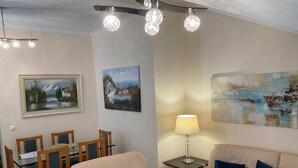 Uma sala de estar com um sofá bege, uma mesa de jantar com cadeiras e obras de arte nas paredes.