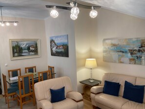 Ein Wohnzimmer mit einem beigefarbenen Sofa, einem Esstisch mit Stühlen und Kunstwerken an den Wänden.