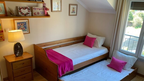 Quarto com cama de madeira, mesa de cabeceira, luminária e janela.