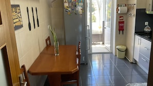 Uma cozinha com mesa de jantar, cadeiras, geladeira e um relógio na parede.
