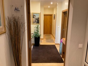 Ein Flur mit einer Holztür, einem Blumentopf, einem gerahmten Bild an der Wand und einem Teppichboden.
