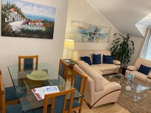 Ein Wohnzimmer mit einem Glastisch, einem beigefarbenen Sofa und einem Gemälde mit einer Küstenlandschaft.