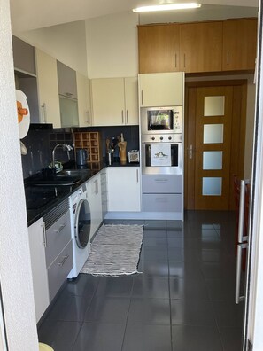 A modern kitchen with a washing machine, a microwave, and a stove. - Moniz Apartment - Caniço (Santa Cruz)
