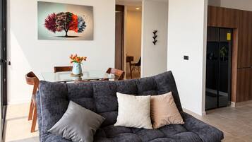 Un salon moderne avec un canapé gris foncé, une table basse en verre et un tableau représentant un arbre accroché au mur.