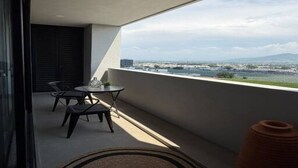 A balcony with a table and chairs, overlooking a body of water and distant buildings.