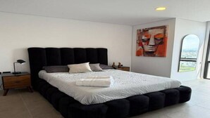 A modern bedroom with a large bed, a nightstand, a lamp, and a city view through a window.