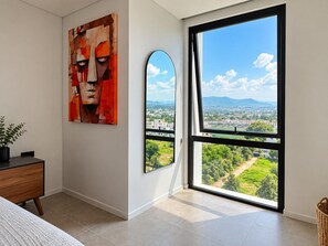 Un dormitorio con un ventanal grande, un cuadro y vistas a un paisaje urbano.