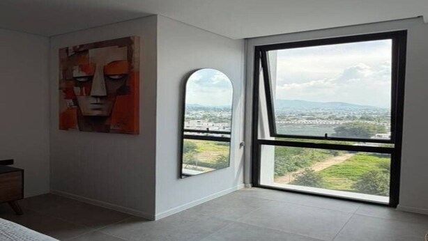 A room with a large window, a painting on the wall, and a bed.