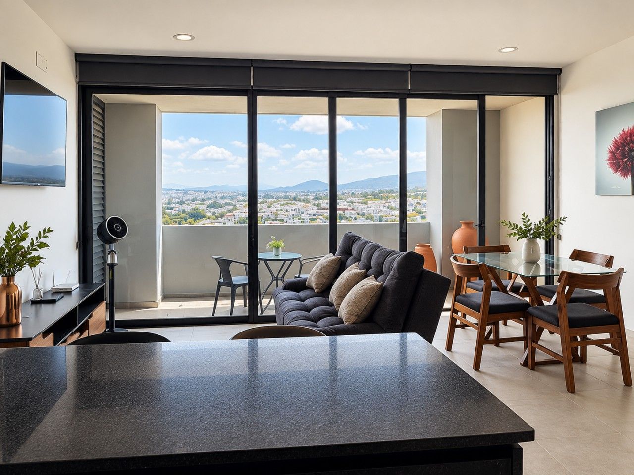 A modern living space with a large window, a sofa, a dining table, and a TV mounted on the wall.
