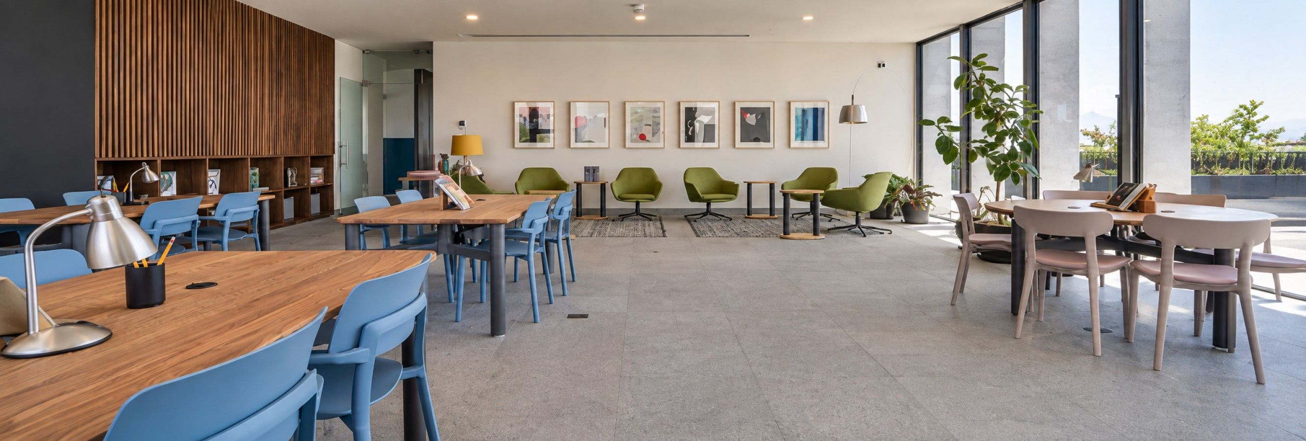 Ein moderner Essbereich mit Holztischen und blauen Stühlen, einer Wand mit Holzlamellen und gerahmten Kunstwerken.