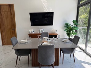 Un comedor moderno con una mesa grande dispuesta para cuatro personas, un televisor de pantalla plana en la pared y una planta en maceta cerca de la ventana.