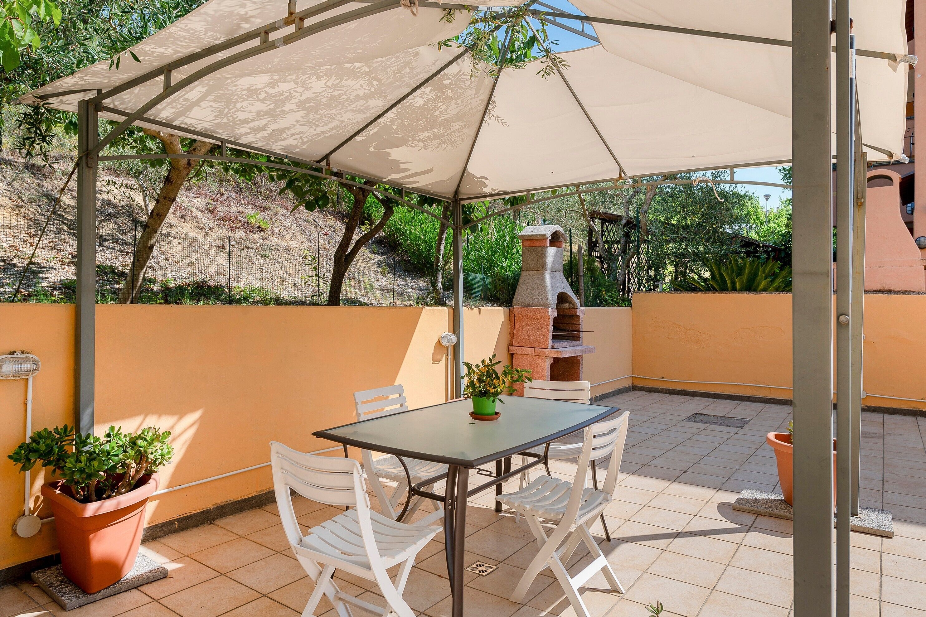 An outdoor patio with a table and chairs, a barbecue grill, and potted plants.