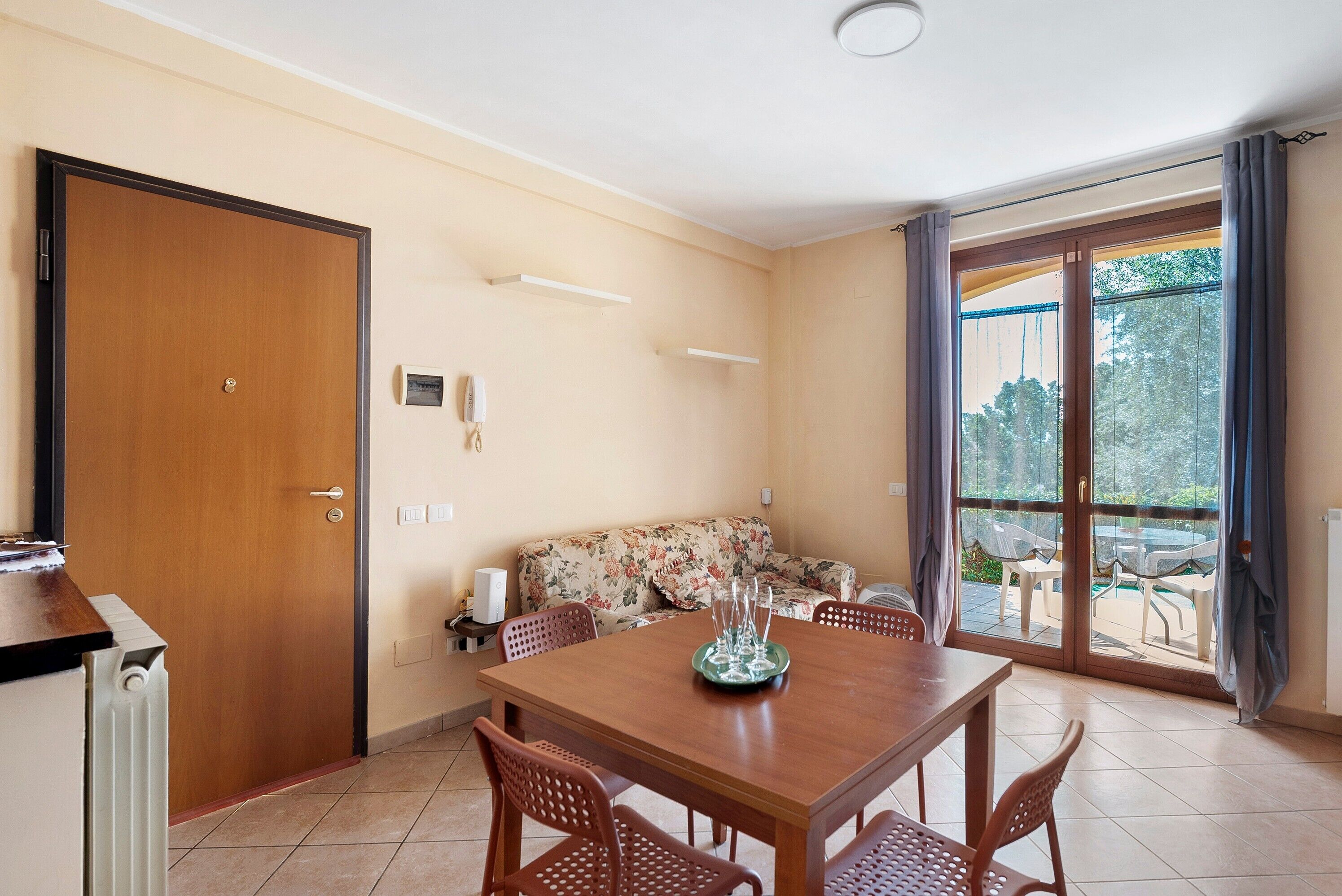 Un'area pranzo con un tavolo e sedie in legno, un divano e una porta scorrevole in vetro che dà su uno spazio esterno.