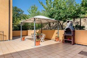 An outdoor patio with a covered seating area, a barbecue grill, and potted plants.
