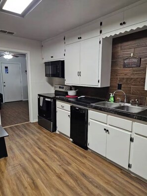 A modern kitchen with white cabinets, a black countertop, and a wooden backsplash.