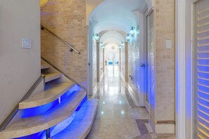 A hallway with a staircase leading to a door, a tiled floor, and a light fixture on the wall. - Luxury 6BR Beach Front House In Fort Lauderdale (Fort Lauderdale)