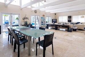 Un vaste espace de vie comprenant un coin repas avec une table à plateau en verre, entourée de chaises, d’un canapé et d’un téléviseur.