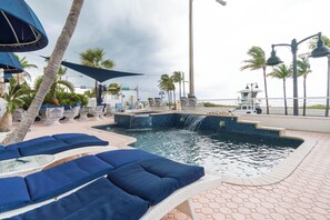 A poolside area with lounge chairs, a small waterfall feature, and a view of the ocean. - Luxury 6BR Beach Front House In Fort Lauderdale (Fort Lauderdale)