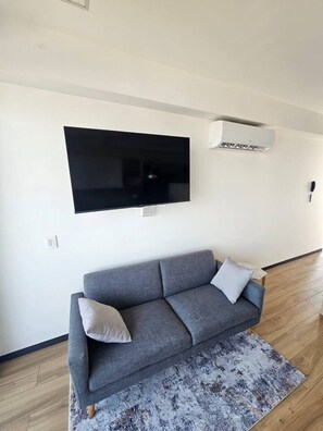 A modern living room with a grey sofa, a mounted flat-screen TV, and a patterned rug on a wooden floor. - Torre Nous | A Pasos de Chapultepec+Seguridad 24/7 (Guadalajara)
