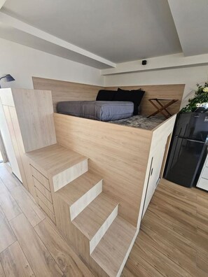 Un dormitorio moderno estilo loft con cama empotrada, una pequeña kitchenette y una escalera.