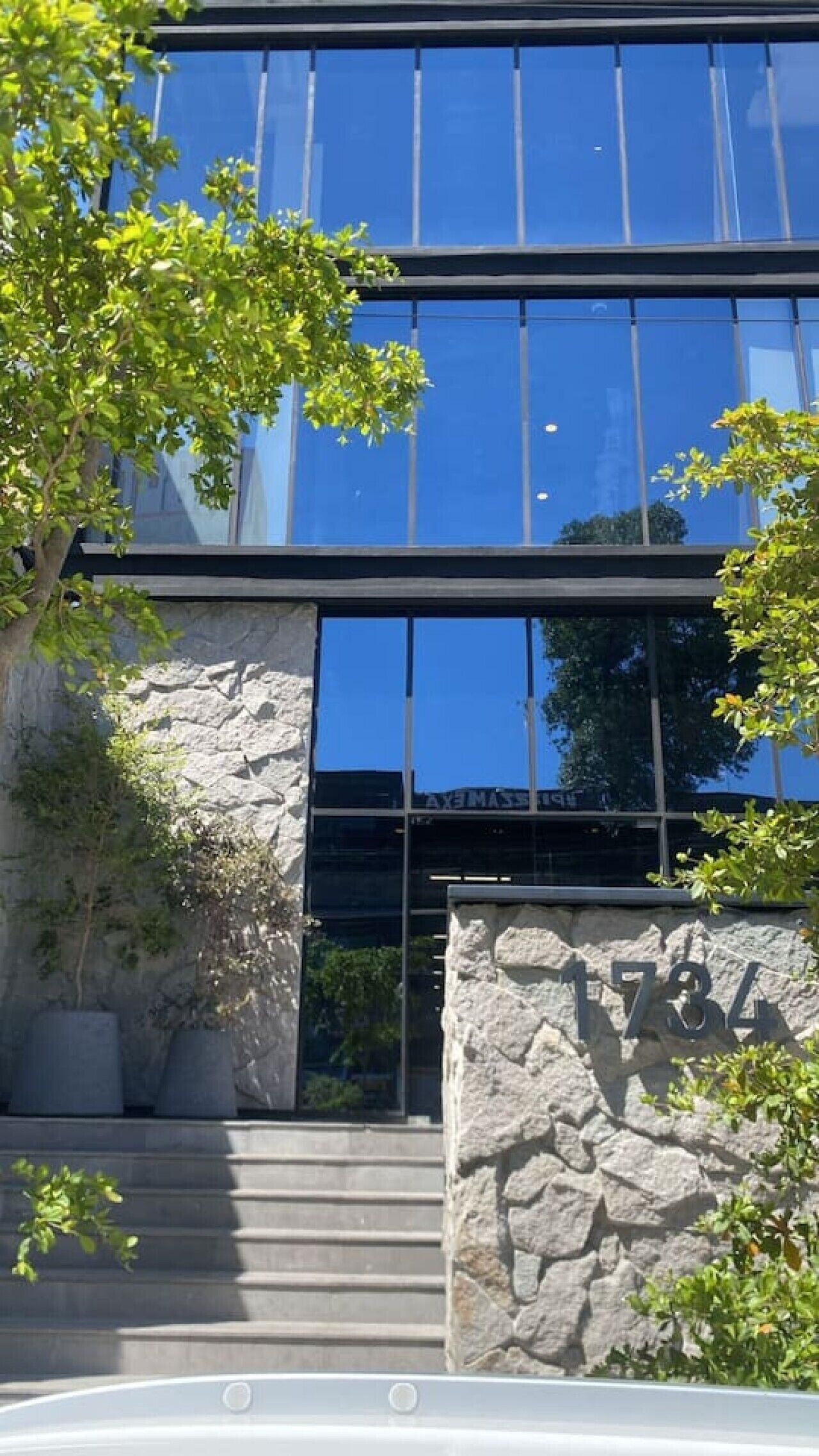 A modern building with a stone facade, large glass windows, and a staircase leading to the entrance.