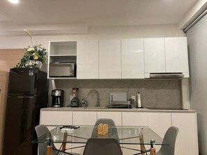 A modern kitchen with white cabinets, a black refrigerator, a coffee maker, and a glass dining table with chairs. - Torre Nous | A Pasos de Chapultepec+Seguridad 24/7 (Guadalajara)