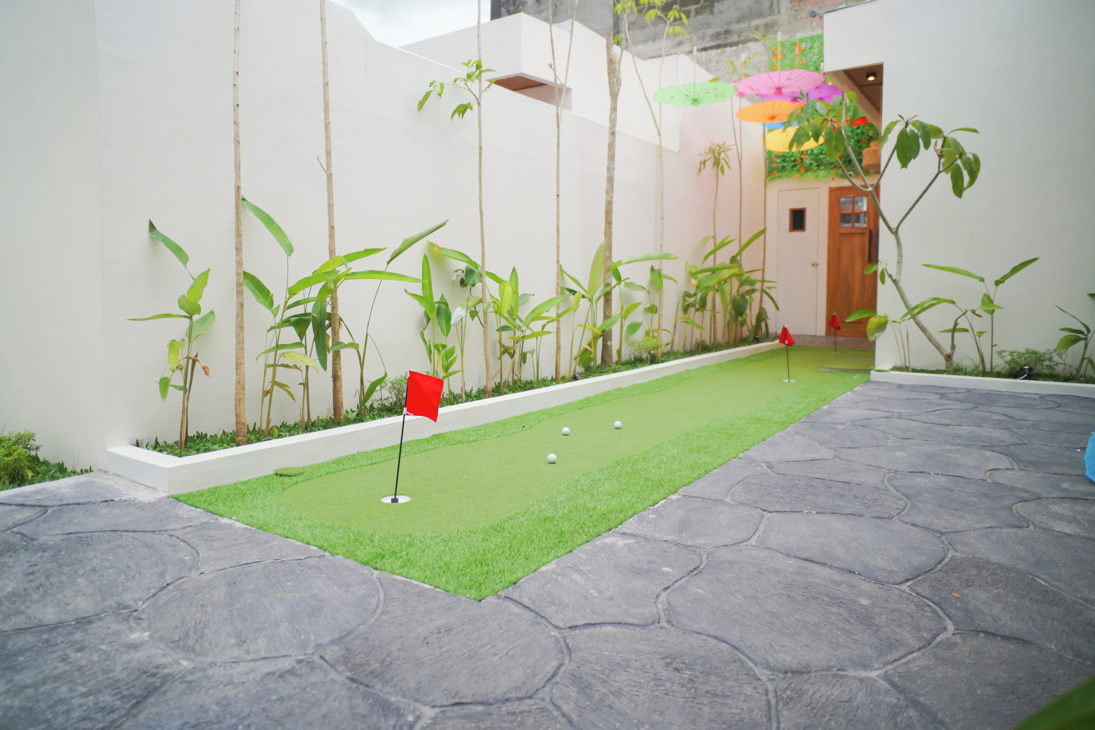A miniature golf course with a green putting area, a red flag, and a stone-tiled path.
