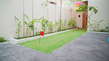 A miniature golf course with a green putting area, a red flag, and a stone-tiled path.