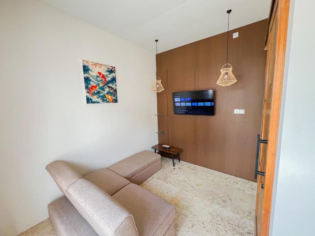 Una habitación con sofá, televisor de pantalla plana en una pared de madera y dos lámparas colgantes.