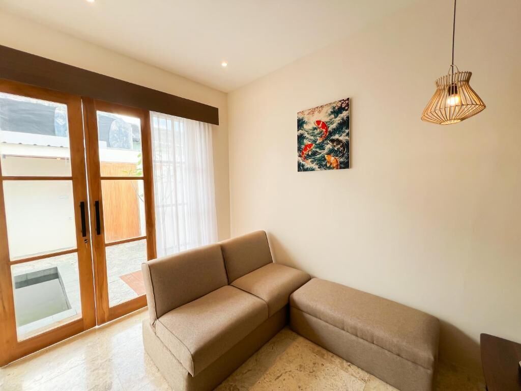 Een moderne woonkamer met een beige hoekbank, een glazen schuifdeur naar een buitenruimte en één kunstwerk aan de muur.