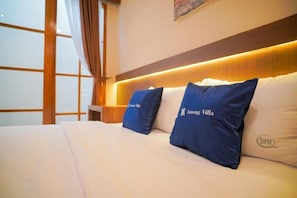 Een hotelkamer met een bed, twee met branding voorzien kussens, een nachtkastje en een raam met gordijnen.