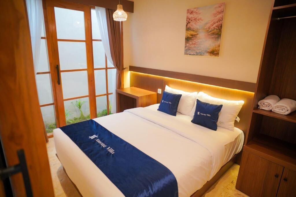 Een hotelkamer met een bed, nachtkastje, plank met handdoeken en een raam met gordijnen.