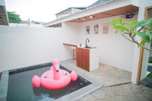 A swimming pool with a pink inflatable flamingo, a small bar area, and a plant.