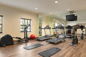 Un gimnasio con equipo de ejercicio que incluye cintas de correr, una elíptica y una bicicleta estática.