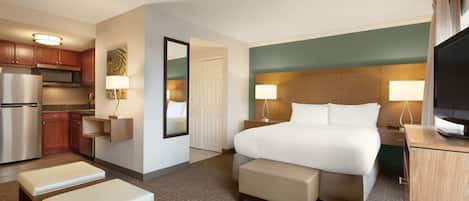 A hotel room with a bed, bedside tables, a TV, a kitchenette, and a bathroom.