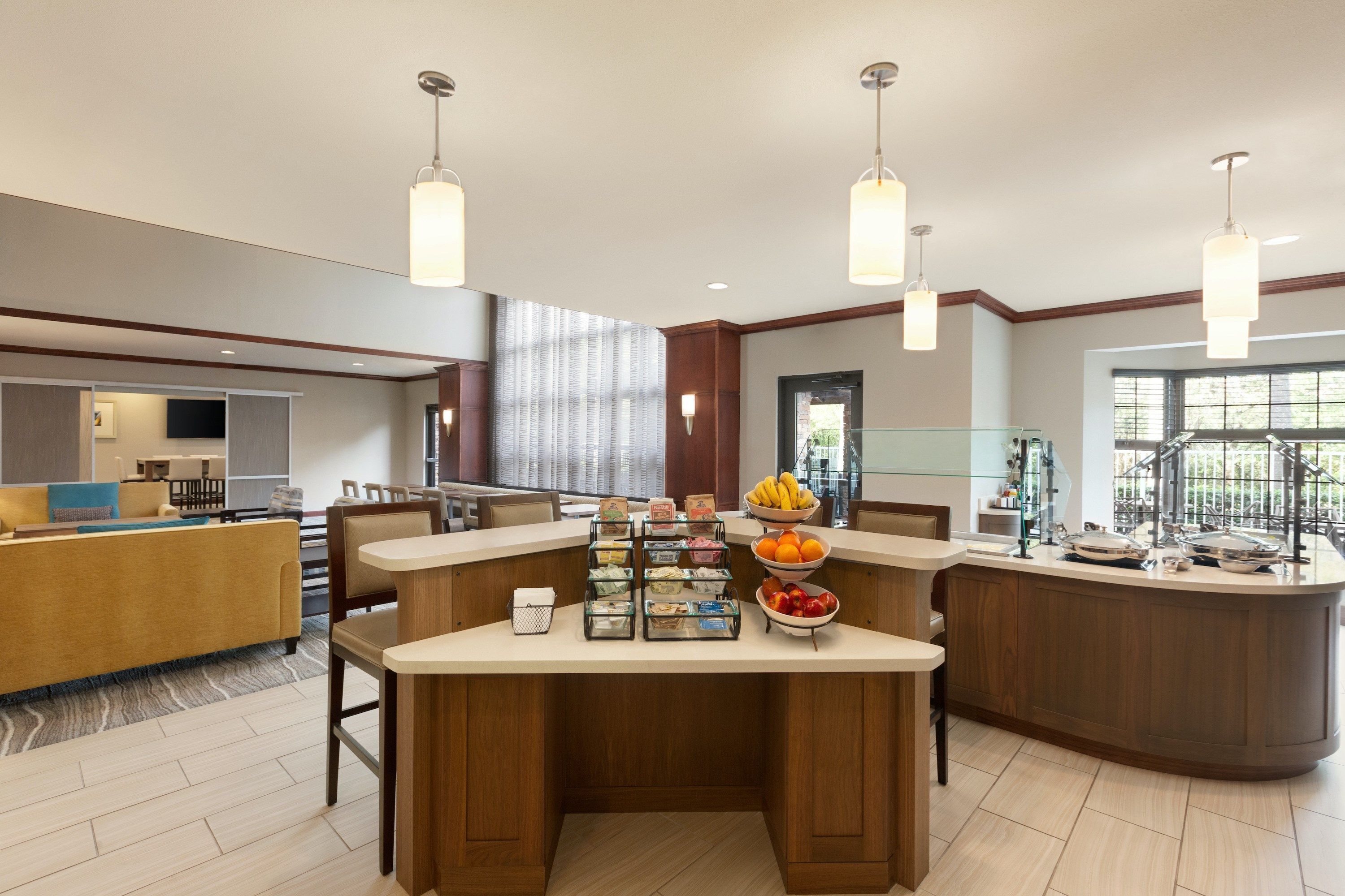 A modern hotel lobby with a central bar area, seating arrangements, and a large window providing natural light.