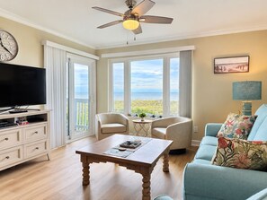 A living room with a television, a wooden coffee table, a sofa, and a ceiling fan. - 3BR Direct Ocean Front Condo @ The Point! Point Emerald Villas A209 (Emerald Isle)