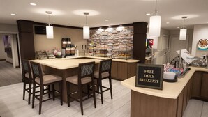 A breakfast bar with a sign offering free daily breakfast, surrounded by chairs and a stone wall.