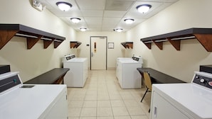 A laundry facility with two rows of washing machines, a door in the center, and wooden shelves above the machines.