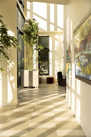 Ein modernes Interieur mit einem Schachbrettmuster-Boden, einer großen Topfpflanze, einer Glastür und einem gerahmten abstrakten Gemälde.