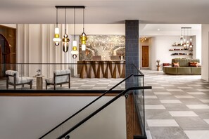 A hotel lobby with a checkered floor, a reception desk, and a seating area with a sofa and chairs.