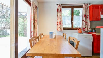 Un coin repas avec une table et des chaises en bois, un petit réfrigérateur et des placards rouges.