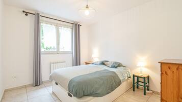 Une chambre à coucher avec un lit, des lampes de chevet, un radiateur, une fenêtre avec des rideaux et une armoire en bois.