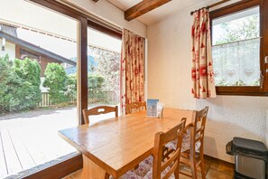 Ein Holztisch mit vier Stühlen, ein Fenster mit Vorhängen und Blick auf ein bewaldetes Gebiet.