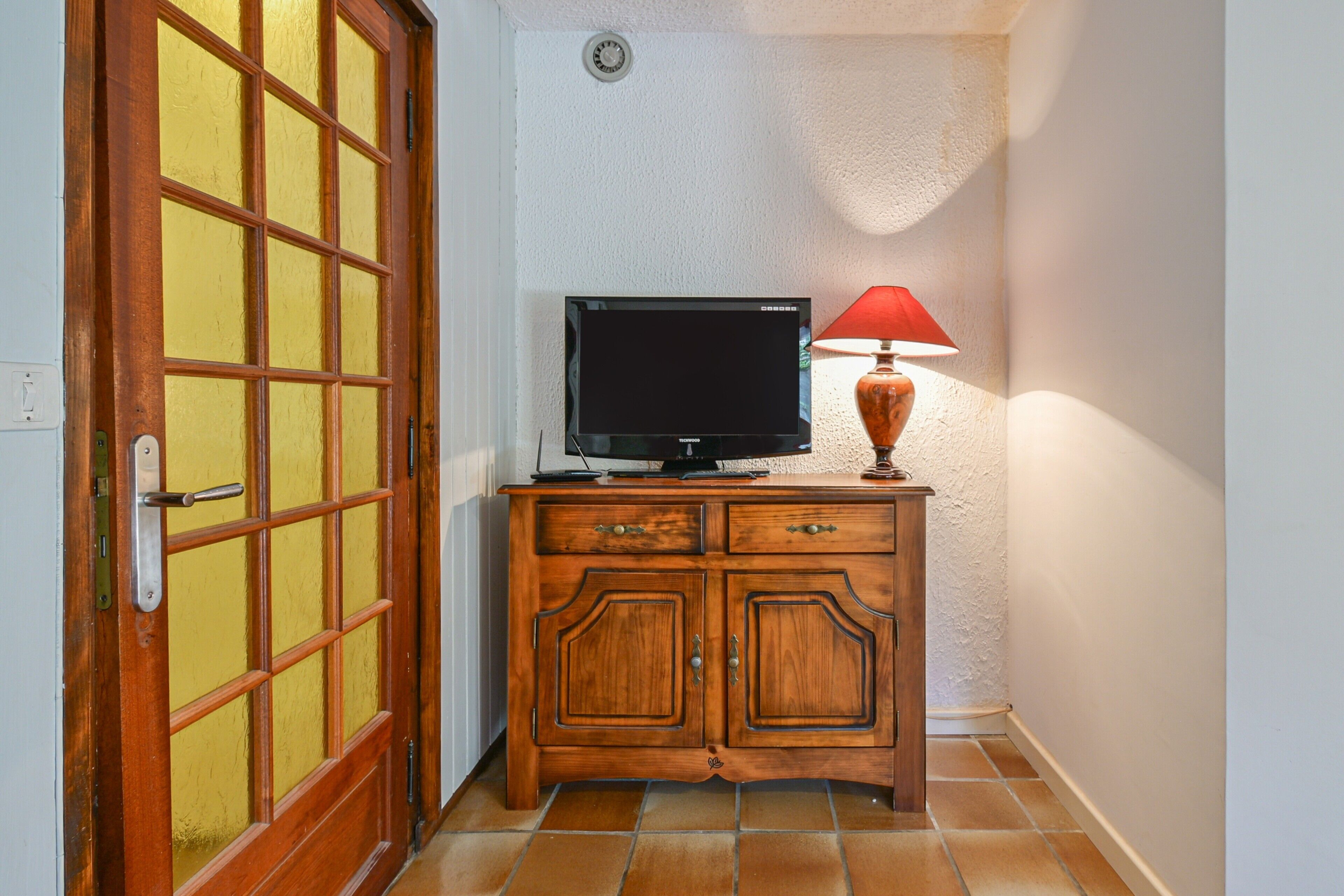 Een houten kast met een televisie erbovenop, een rode lamp en een deur met een ruitpatroon.