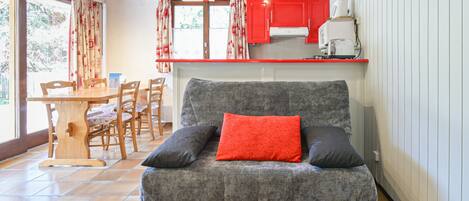 Un espacio de sala acogedor con un sofá, una mesa de comedor con sillas y una cocina con armarios rojos.