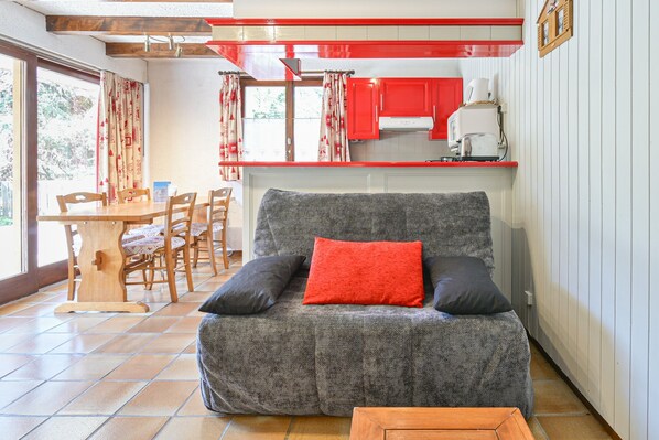 Ein gemütlicher Wohnbereich mit einer Couch, einem Esstisch mit Stühlen und einer Küche mit roten Schränken.