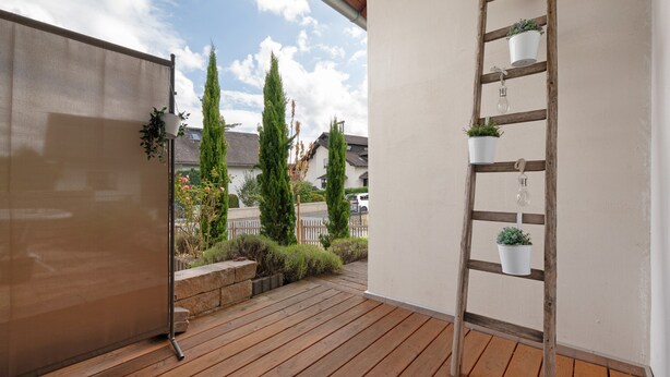 A wooden deck with a metal railing, potted plants, and a view of a residential area with houses and trees.