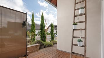 A wooden deck with a metal railing, potted plants, and a view of a residential area with houses and trees.