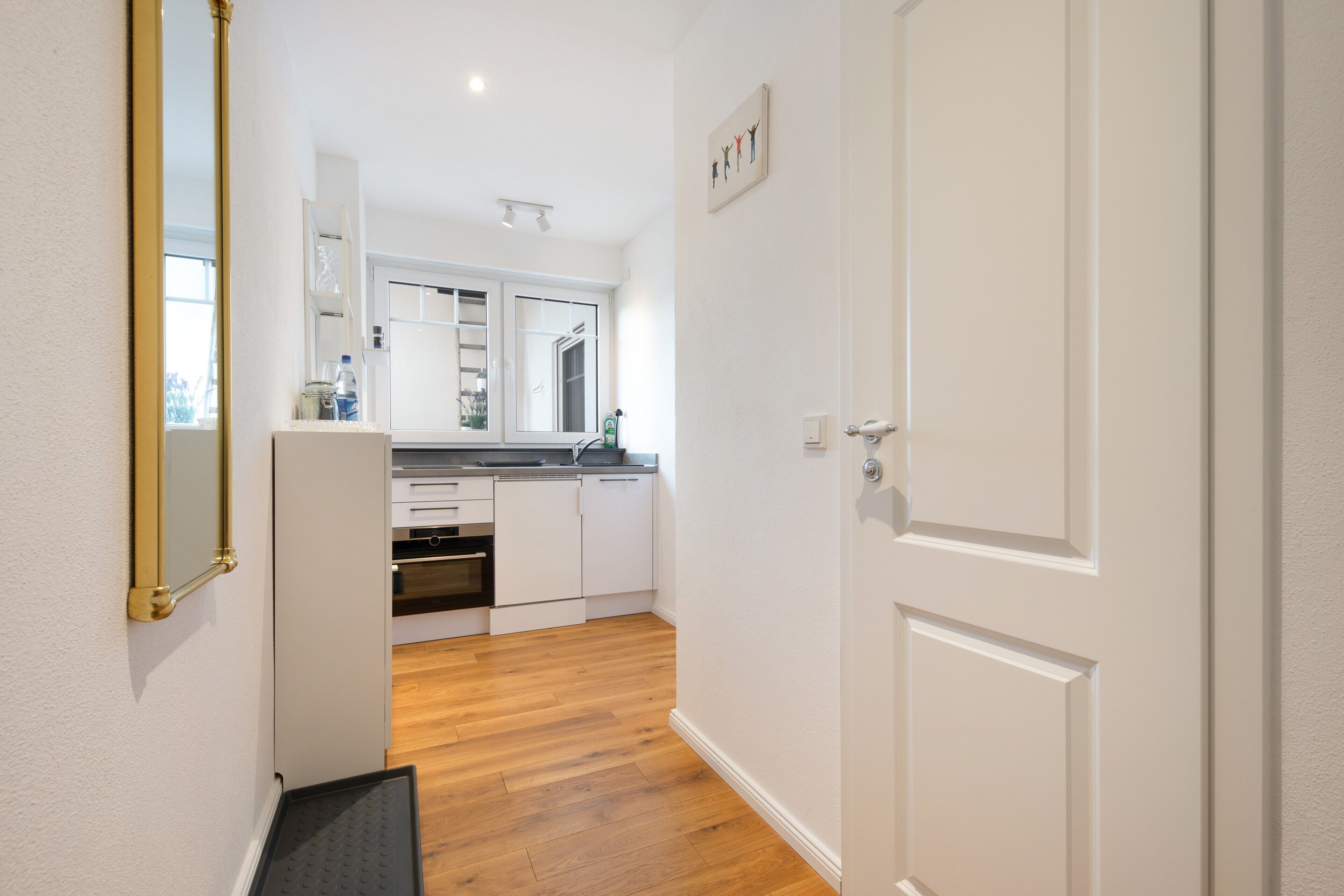 A narrow hallway leading to a kitchen with white cabinets, a countertop, and a window.